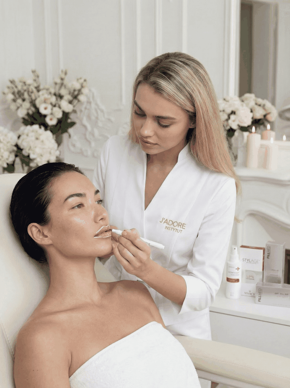 Specjalistka J'ADORE nakłada krem STYL na usta klientki — produkty do pielęgnacji ust na stoliku